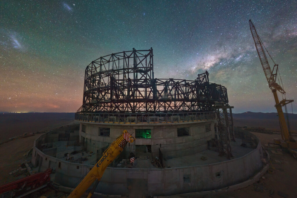 En webbkamerabild från juni 2023 som visar bygget av ESO:s ELT vid Cerro Armazones i Atacamaöknen, Chile. Den spektakulära himmelsbakgrunden domineras av Vintergatans centrum och det Stora och Lilla Magellanska molnet, två av dvärggalaxerna som kretsar kring Vintergatan. Källa: ESO